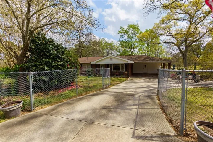 View of front of property featuring concrete driveway, a carport, a fenced front yard, and a gate