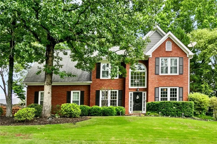 Traditional brick exterior with gabled roofline, mature trees, manicured lawn, and foundational landscaping