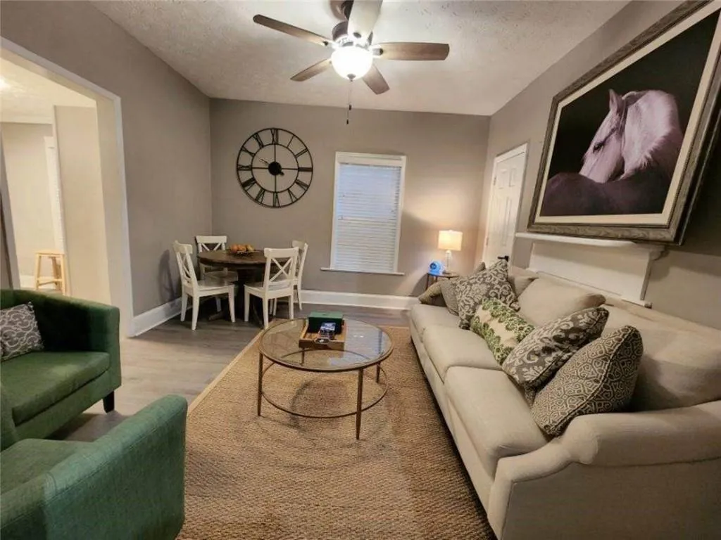 Living area with a textured ceiling, baseboards, a ceiling fan, and light wood-style flooring