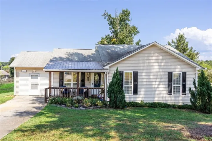 Siding exterior with a covered porch, dark window shutters, an attached garage, and a concrete driveway