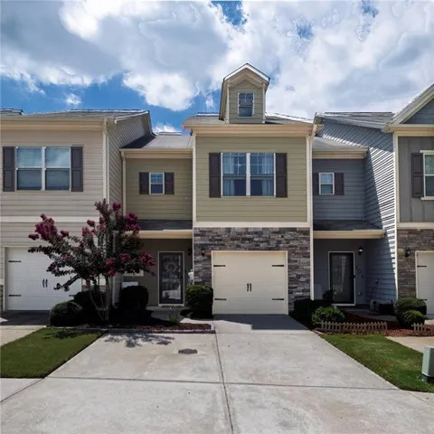 Multi-level exterior with dormer window, stone accent siding, attached garage, and concrete driveway