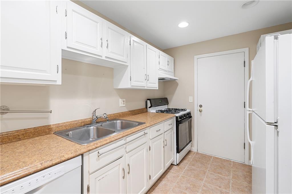 Kitchen featuring white cabinets, light tile floors, white appliances, and sink