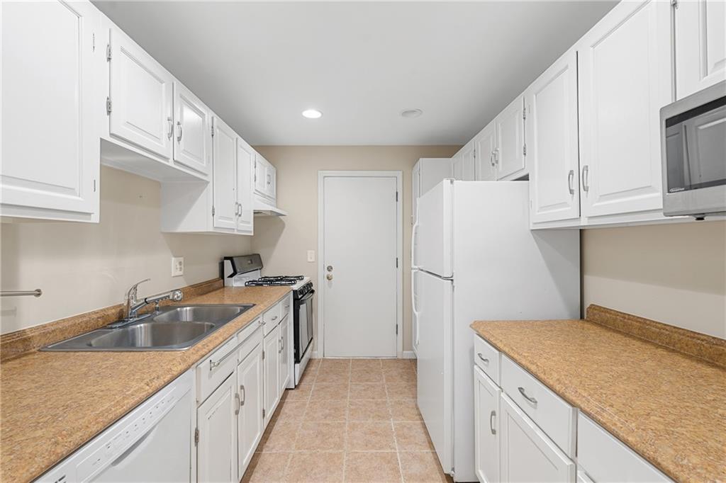 Kitchen with sink, white appliances, light tile flooring, and white cabinets