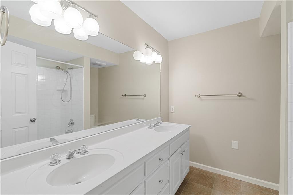 Full bathroom with vanity with extensive cabinet space, toilet, tile flooring, double sink, and tiled shower / bath combo