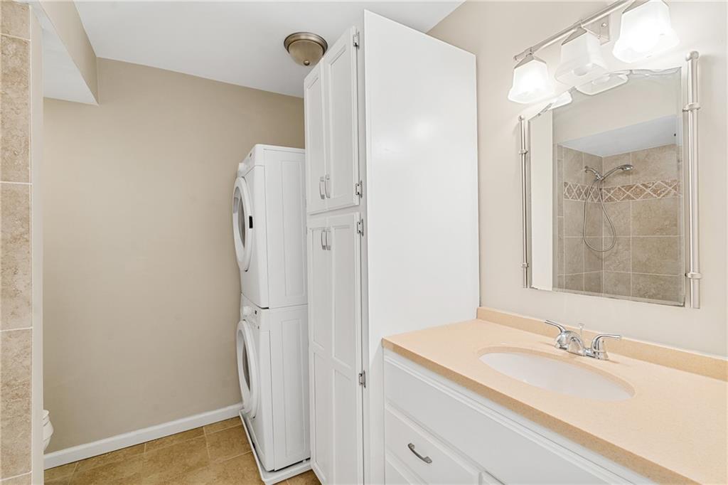 Bathroom featuring stacked washer / dryer, toilet, vanity with extensive cabinet space, and tile floors
