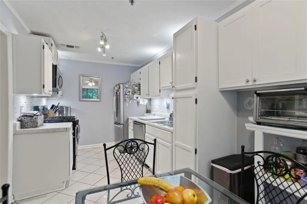 Kitchen featuring appliances with stainless steel finishes, white cabinets, light tile patterned flooring, and light countertops