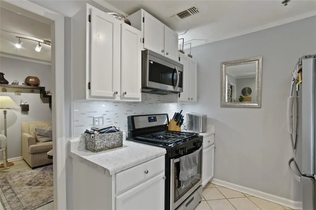 Kitchen with stainless steel appliances, tasteful backsplash, light countertops, white cabinets, and crown molding