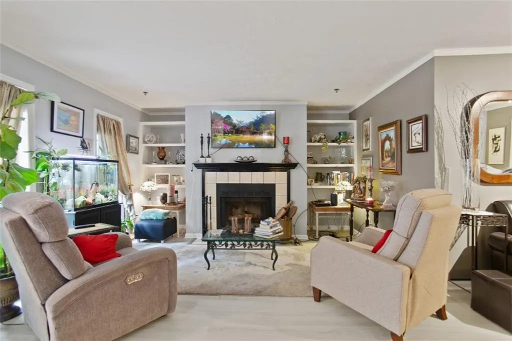 Living room featuring crown molding, a tiled fireplace, wood finished floors, and built in shelves