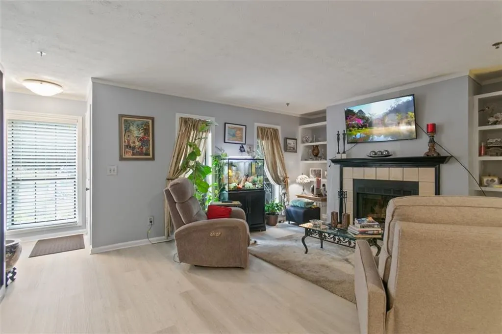 Living room featuring wood finished floors, ornamental molding, a fireplace, a textured ceiling, and built in features
