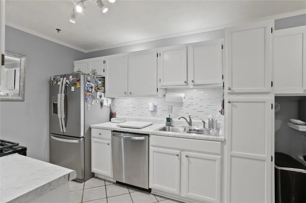 Kitchen featuring appliances with stainless steel finishes, light countertops, white cabinetry, light tile patterned floors, and tasteful backsplash
