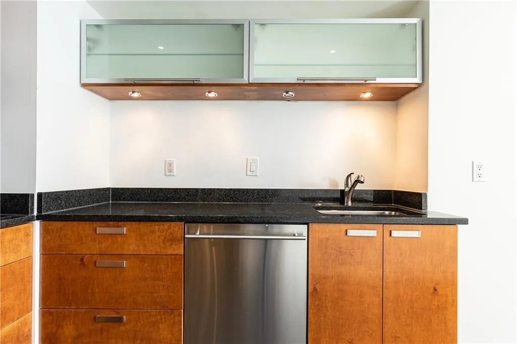 Kitchen featuring stainless steel dishwasher, glass insert cabinets, and dark stone counters