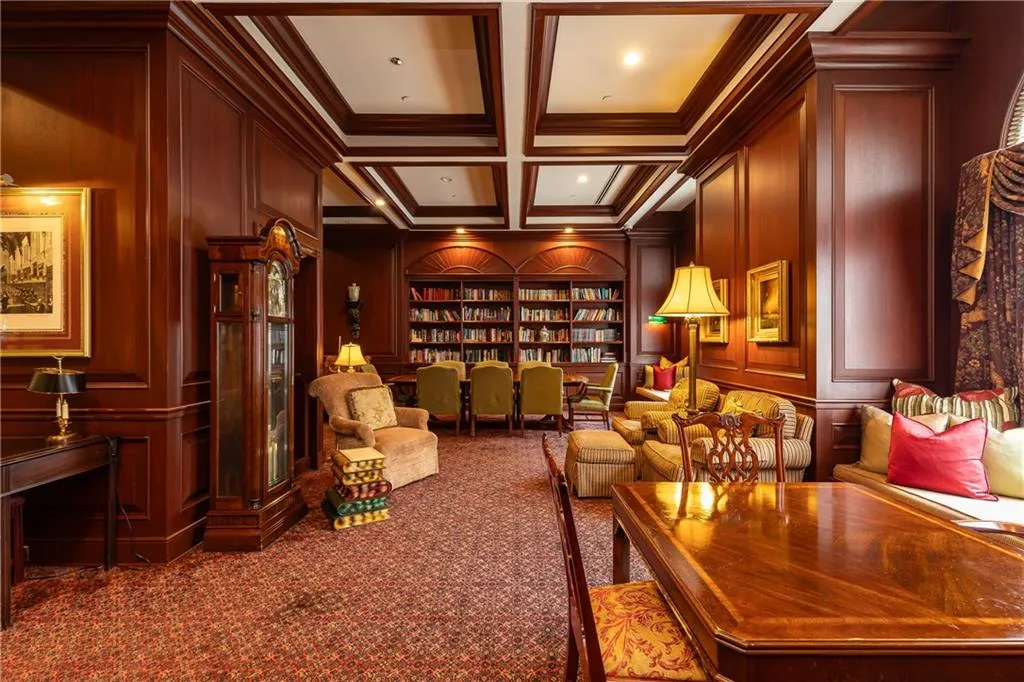 Living area with built in features, ornamental molding, carpet flooring, coffered ceiling, and a decorative wall