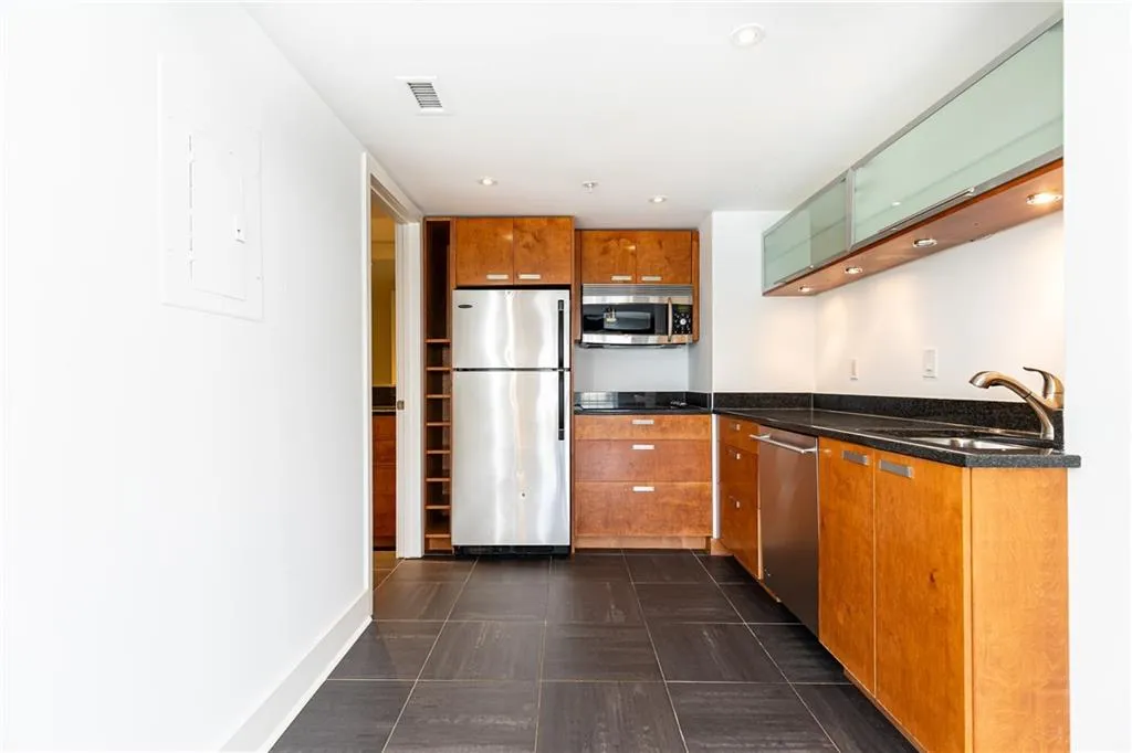 Kitchen with appliances with stainless steel finishes, brown cabinetry, dark stone counters, and recessed lighting
