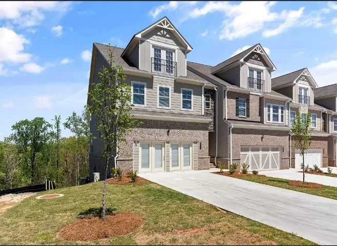 Contemporary townhome featuring a brick and siding exterior, dormer windows with decorative gable accents, and a two-car garage with French doors