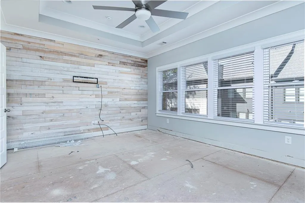 Empty room featuring wood walls, a raised ceiling, ceiling fan, and ornamental molding