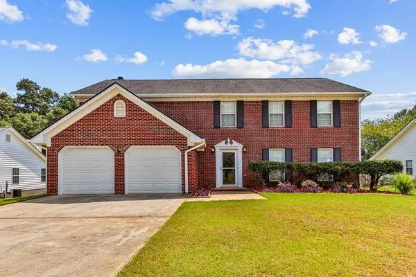 Brick exterior featuring a two-car garage, mature landscaping, and a covered entry