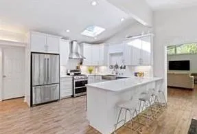 Kitchen with white cabinetry, hood, stainless steel fridge, and light porcelain flooring