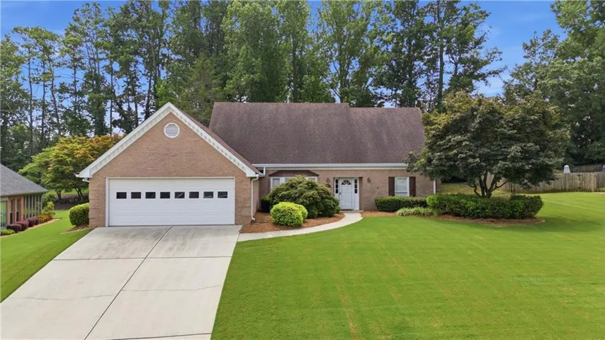 Brick facade with a white front door, a two-car garage, established landscaping, and a concrete driveway