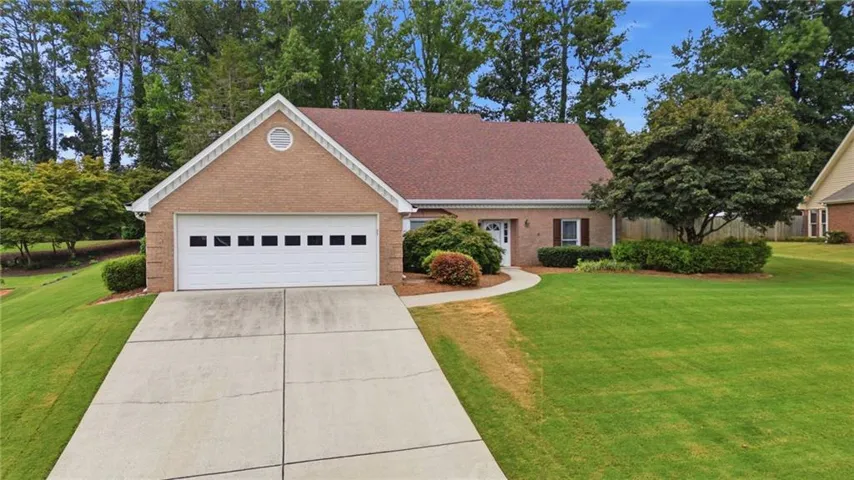 Brick exterior with an attached garage, featuring a concrete driveway, a front entry walk, and a landscaped front yard with mature trees