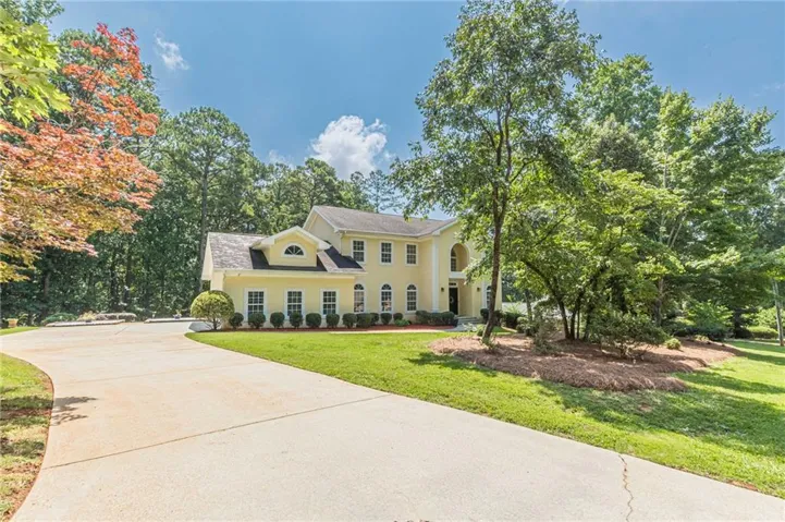 Two-story residence with a yellow stucco exterior, arched entry, multiple windows, a dormer window, and mature landscaping