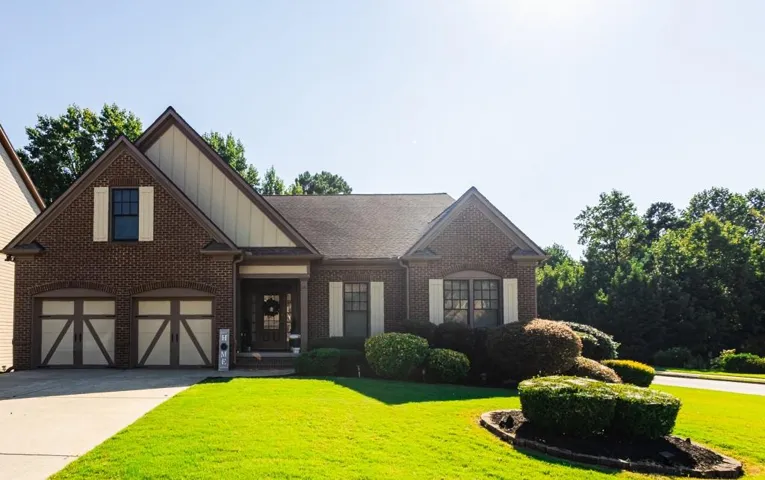 Brick facade with gabled roofline, two-car garage with decorative doors, covered entry porch, and a manicured lawn with established landscaping