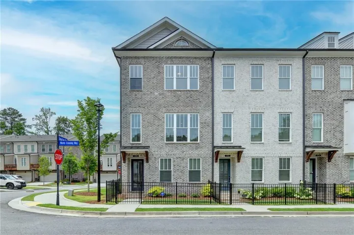 Contemporary townhome featuring a brick facade with light gray and off-white tones, multi-pane windows, and a black wrought iron fence