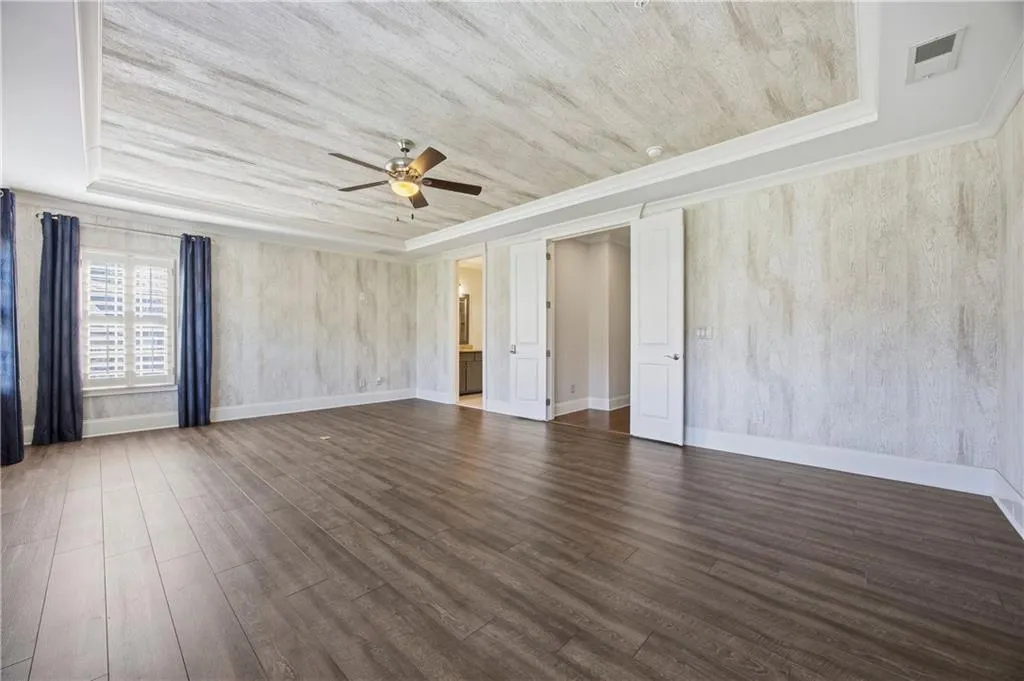 Empty room with a tray ceiling, dark wood-type flooring, ceiling fan, and crown molding
