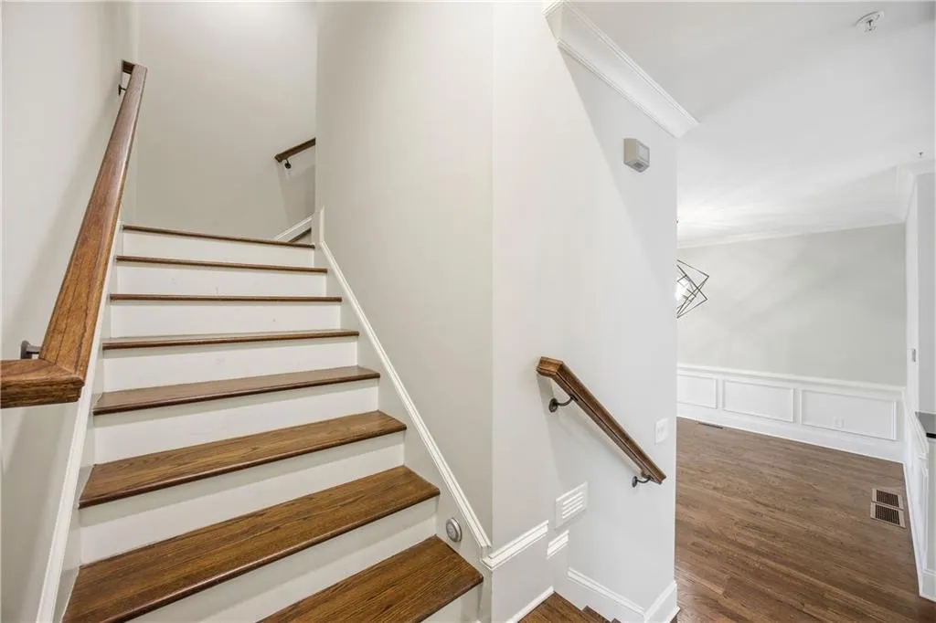 Stairs with wood finished floors, crown molding, a decorative wall, and wainscoting