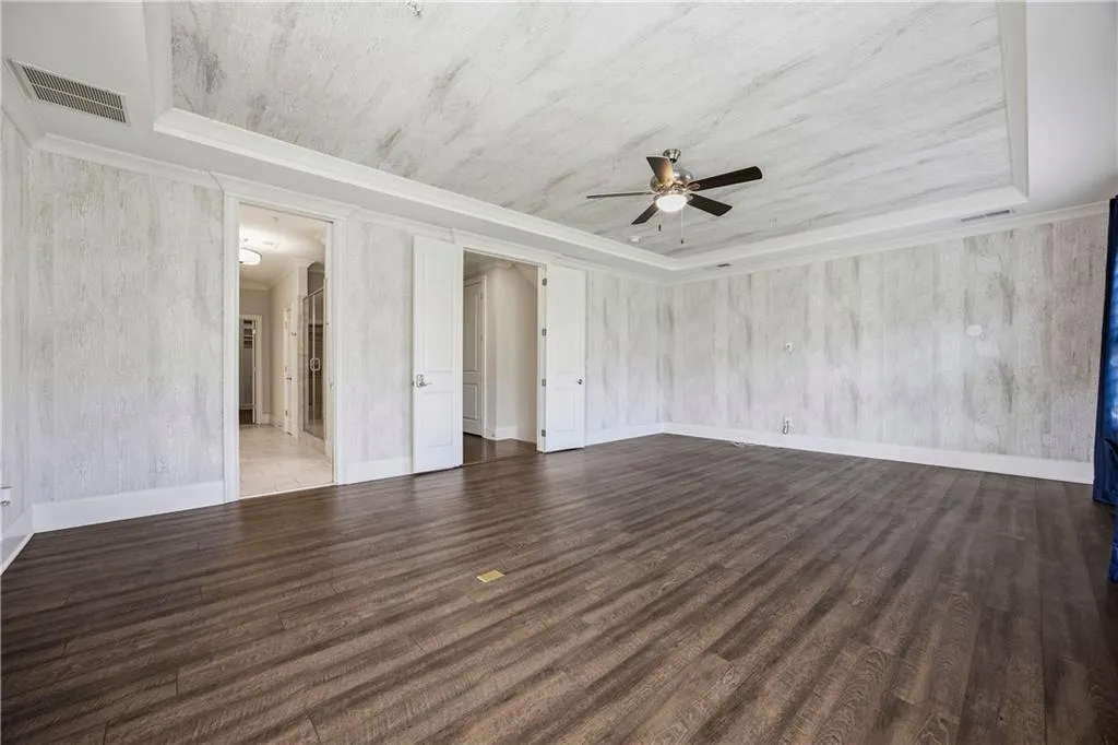 Unfurnished living room featuring a tray ceiling, dark wood-style flooring, and a ceiling fan