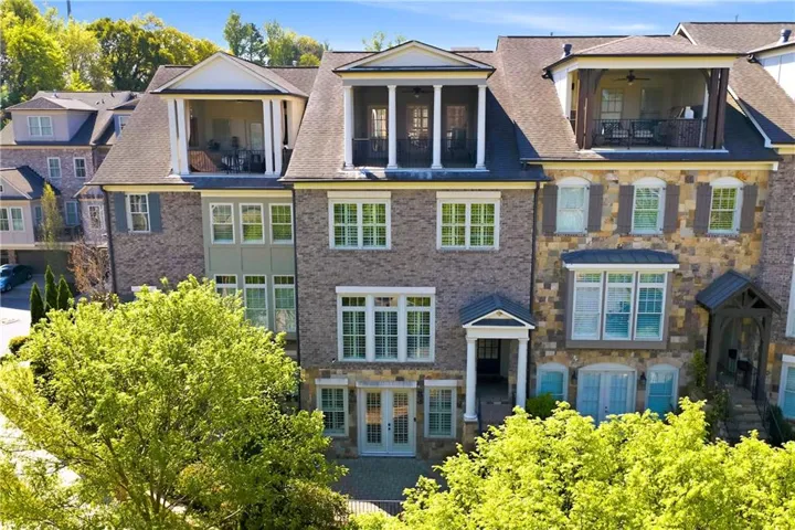 View of front facade with a balcony, brick siding, french doors, and stone siding