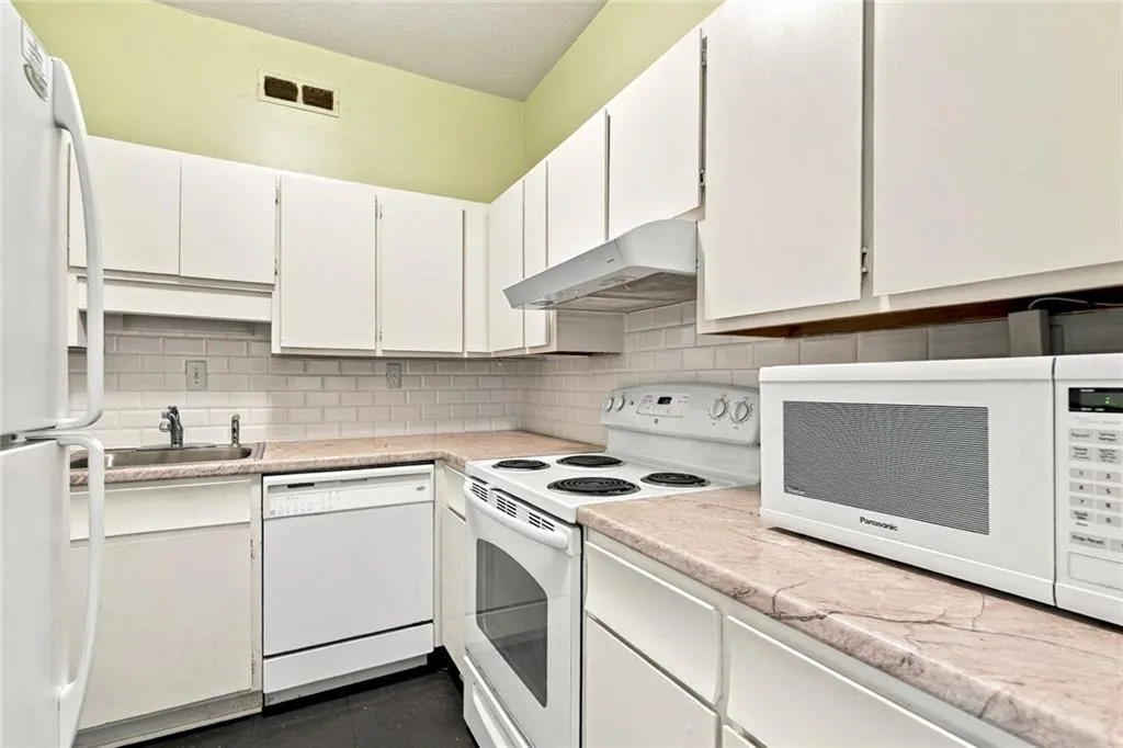 Kitchen featuring white cabinetry, subway tile backsplash, white appliances, and a built-in stainless steel sink