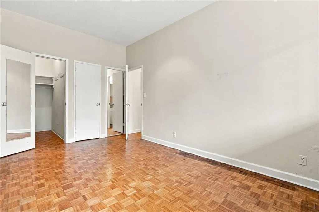 Parquet wood flooring, a built-in closet with shelving, a full-length mirrored door, and neutral wall tones