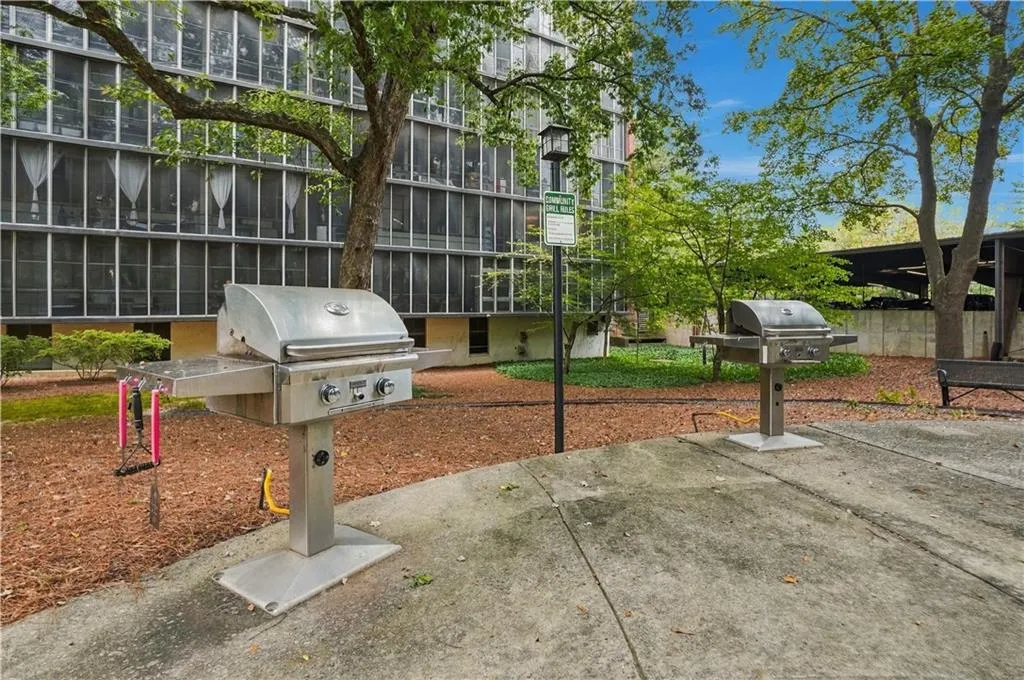 Outdoor grilling stations on a concrete patio, surrounded by mature trees and landscaping