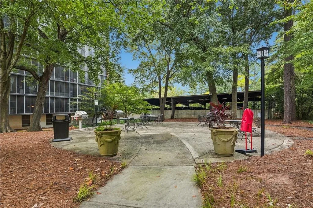 Paved patio area, mature trees, multi-story building exterior, structured landscaping, and a streetlamp