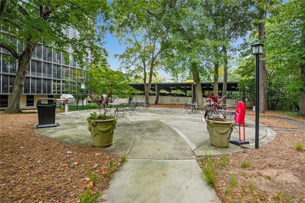 Concrete patio with decorative planters, surrounded by mature trees, featuring a lamppost and a grill station