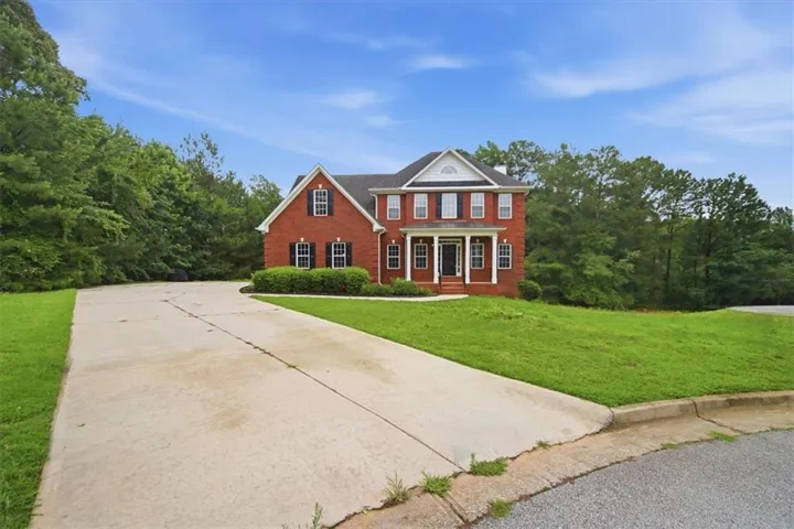 Traditional brick exterior with white columns and shutters, framed by mature trees