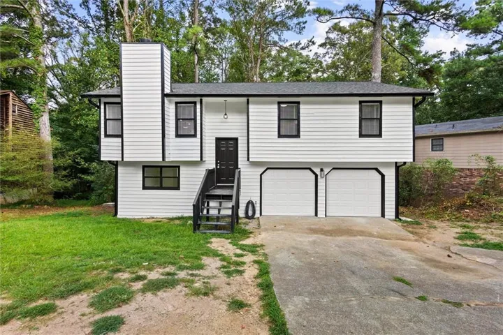 Split-level exterior with white siding and black trim, featuring a two-car garage, front entry steps, and a prominent chimney