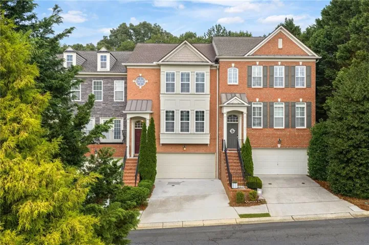 Brick and siding townhome exterior featuring multiple dormer windows, individual garages, covered front entrances with transom windows, and landscaped shrubbery