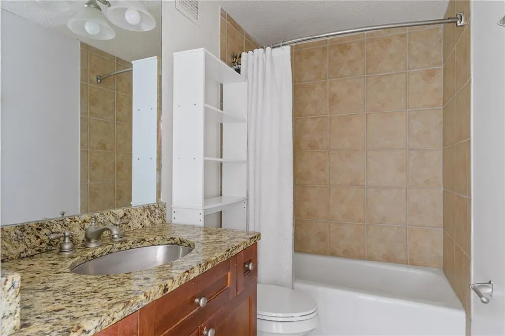 Full bathroom featuring shower / tub combo with granite countertops and chic stainless steel sink.