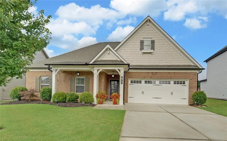 Brick and siding exterior featuring a covered front porch with white columns, an attached garage with a panel door, a concrete driveway, and a manicured lawn with established landscaping