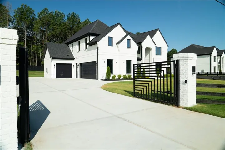 White brick exterior with dark trim accents, a concrete driveway, two black garage doors, and a decorative metal entry gate