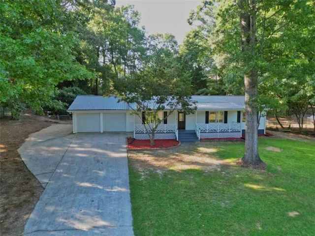 Charming single-story ranch home situated on a spacious, wooded lot with mature trees and plenty of privacy. Features a welcoming covered front porch, metal roof, and attached two-car garage. Large concrete driveway provides ample parking and easy access. The expansive yard offers a combination of open lawn and natural wooded areas, creating a peaceful setting with plenty of outdoor space to enjoy.