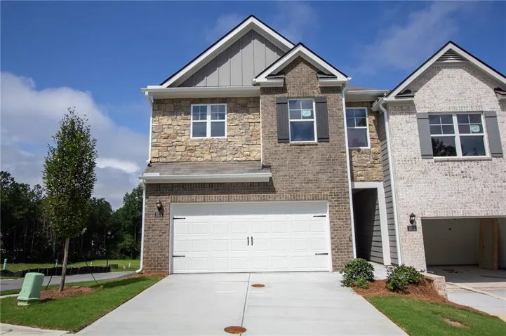 Two-story dwelling featuring a stone and brick façade, white garage door, dark window shutters, and a concrete driveway