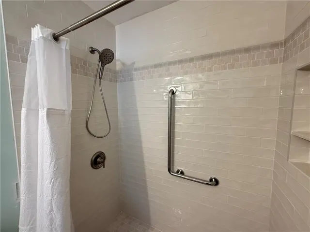 Tiled shower with a handheld showerhead, brushed nickel hardware, built-in shelving, and a mosaic accent tile band