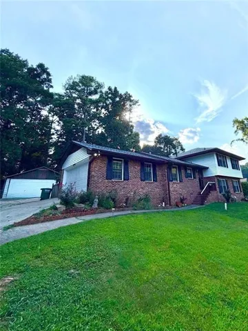 Brick exterior with white siding accents, an attached garage, a detached garage, and a lush green lawn