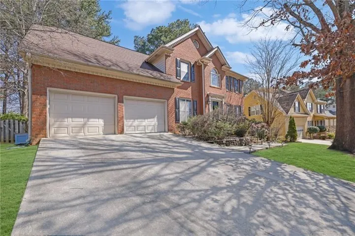 Brick exterior residence featuring a two-car garage, concrete driveway, established landscaping, and a fenced side yard