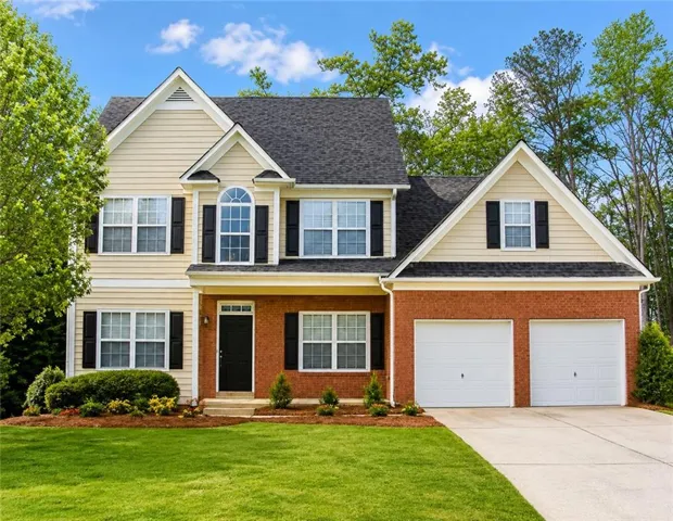 Two-story residence featuring a brick and siding exterior, a two-car garage, and a manicured lawn