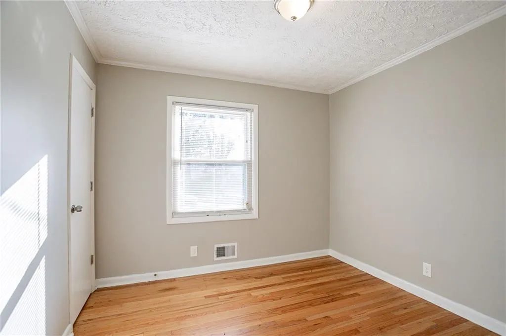 Empty room with visible vents, baseboards, light wood-style flooring, and crown molding