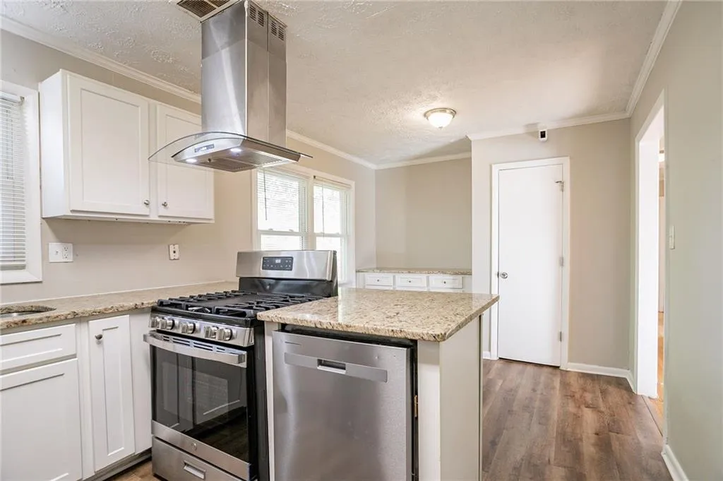 Kitchen featuring wood finished floors, stainless steel appliances, wall chimney range hood, and ornamental molding