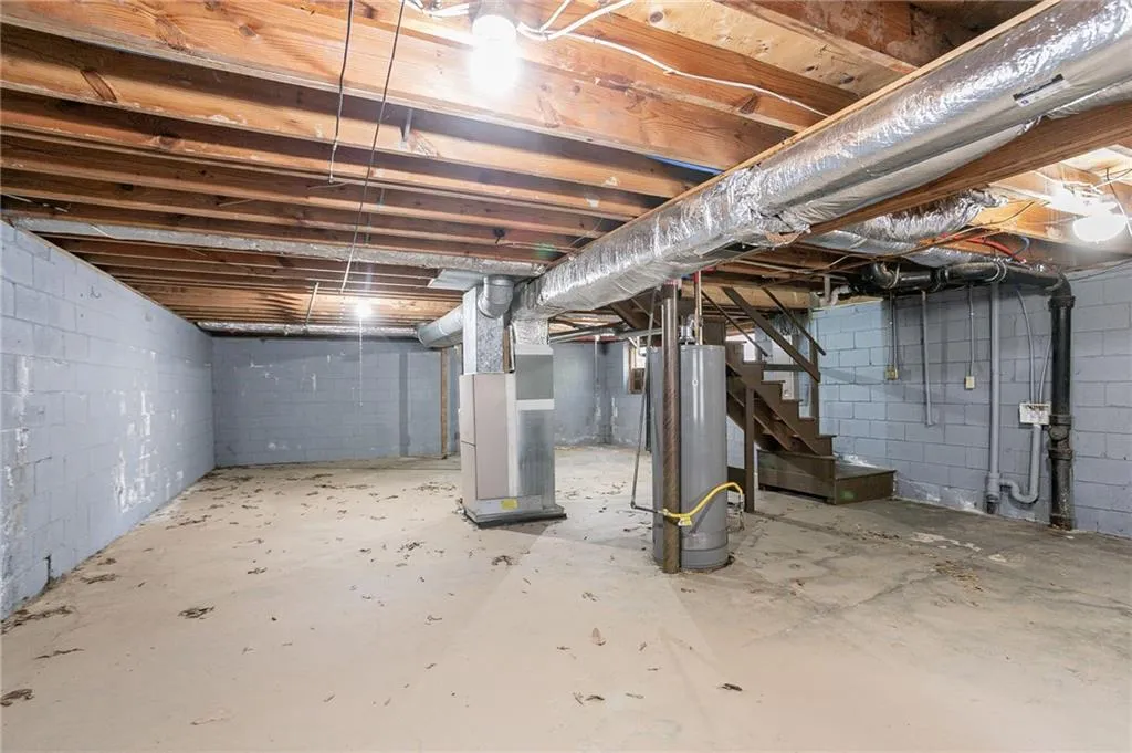Unfinished basement featuring heating unit, stairway, and gas water heater